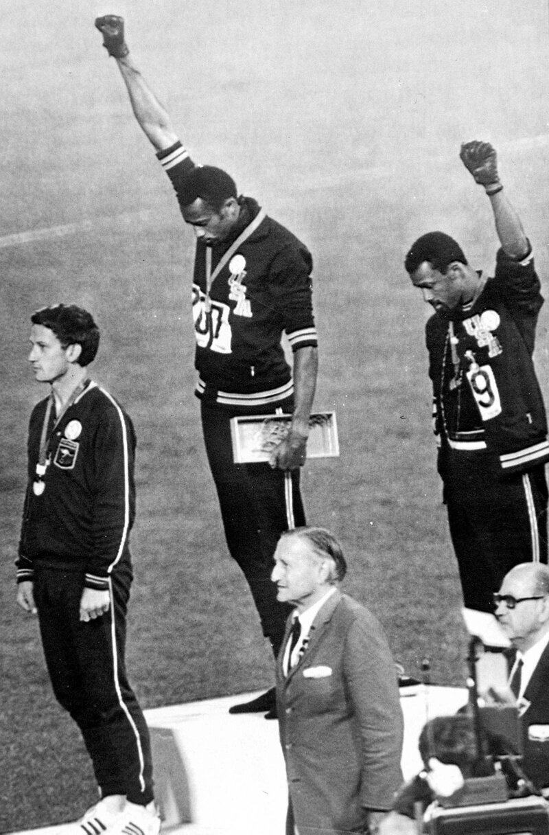 Легкоатлет, олимпийский чемпион Томми Смит (в центре) и бронзовый призер Джон Карлос на награждении подняли кулаки вверх в знак протеста против расизма в США