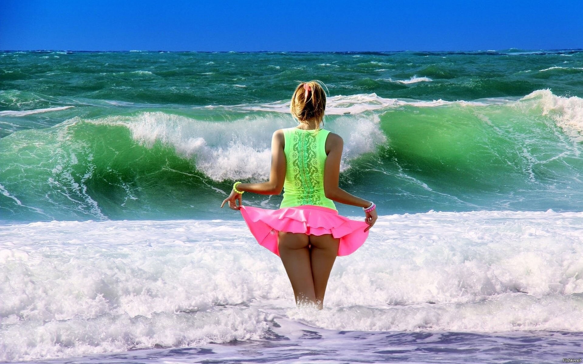 Обнаженная девица с голубыми бусами и парео стоит на берегу моря