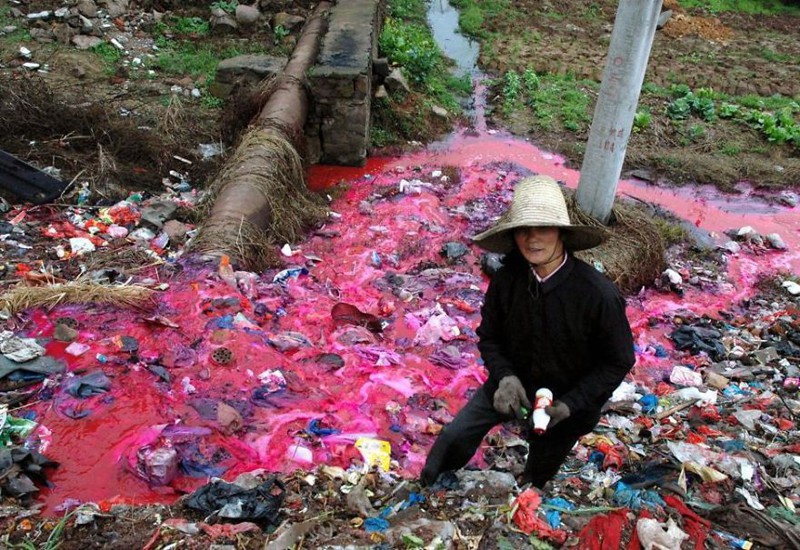 16. Женщина собирает пластиковые бутылки у реки, загрязнённой красным красителем