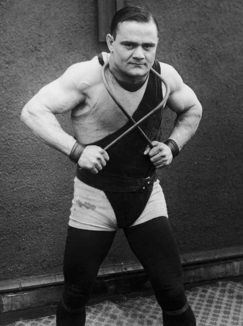 1925 год. Греческий боксер и силач Джаст Лессис демонстрирует свое мастерство, сгибая железный прут вокруг шеи. 