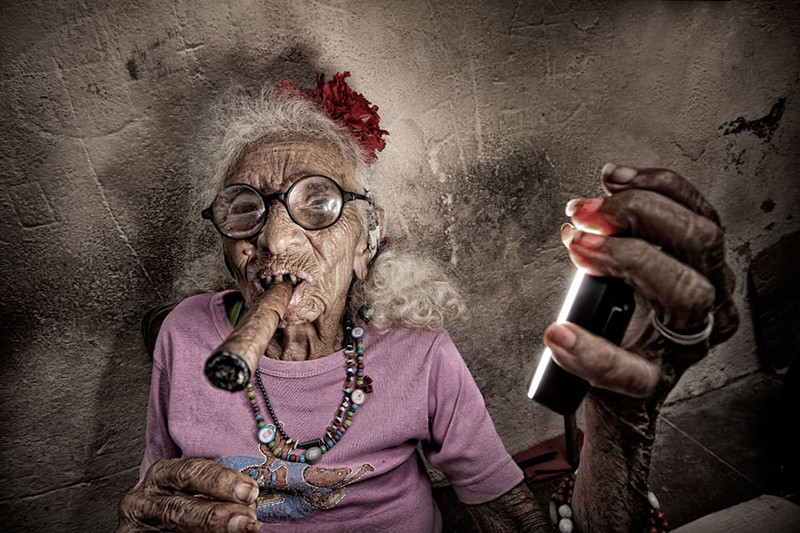 Кубинская женщина курит сигару и держит кольцевую вспышку.