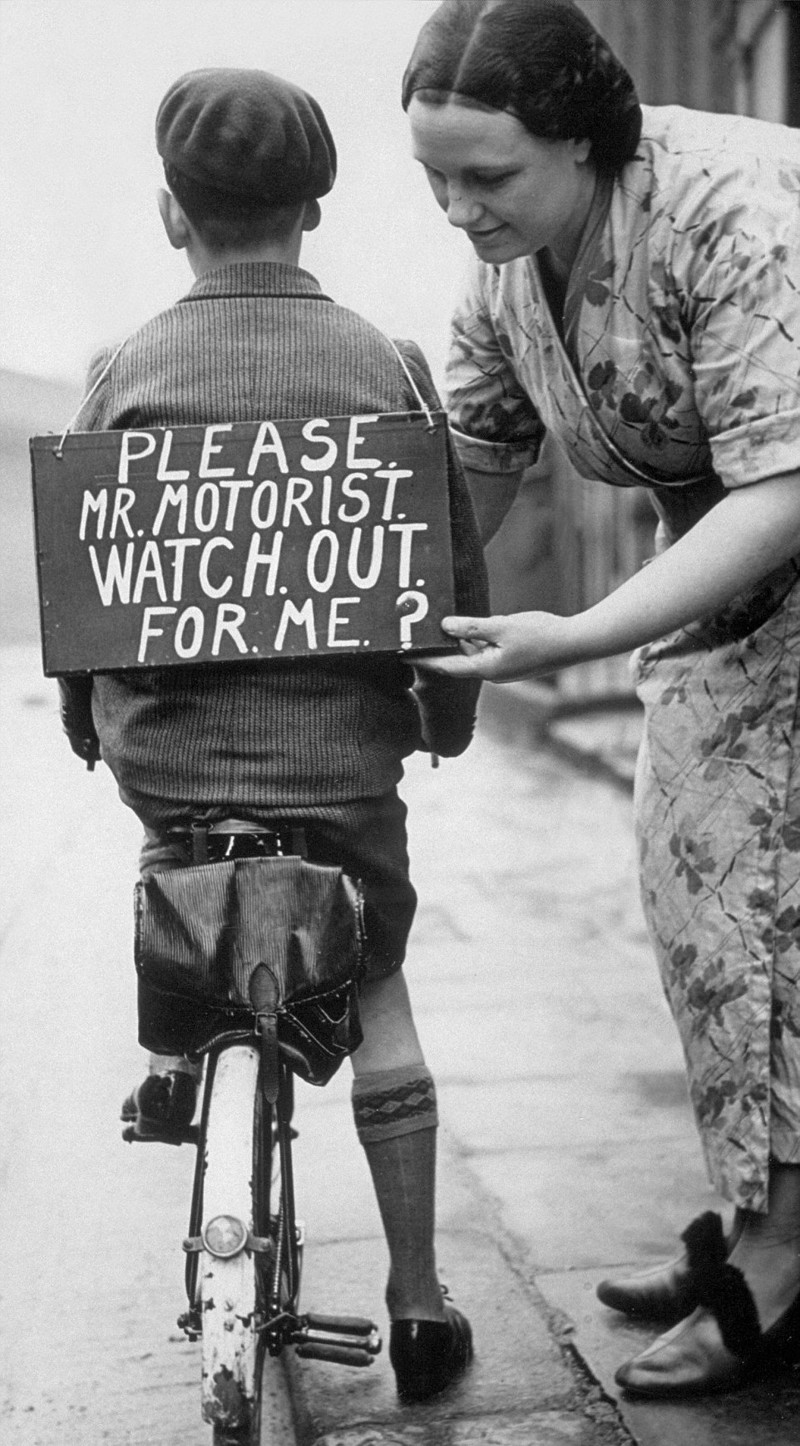 Маленький байкер со знаком на спине с просьбой, чтобы были осторожнее прохожие и автомобилисты.