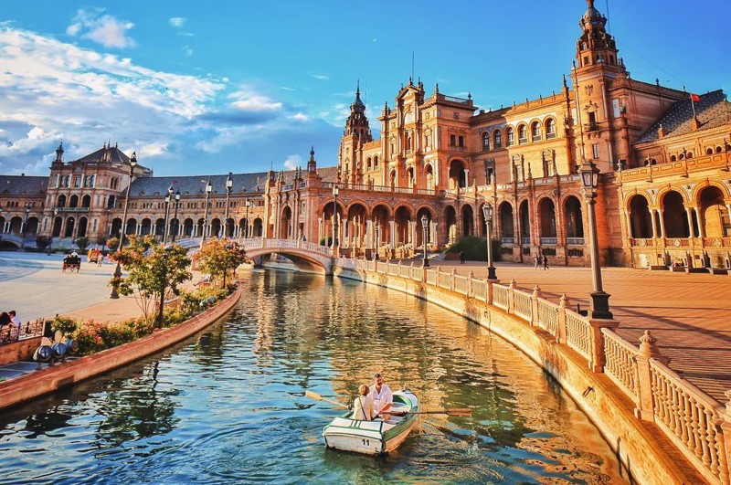 Этот снимок показывает площадь Испании в Севилье, купающуюся в теплом свете в комплекте с романтической поездкой на лодке.
