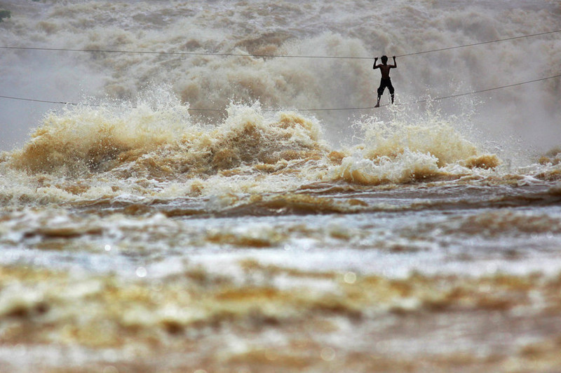 Лаосский рыбак перебирается по мосту, сделанному из натянутых проводов. Он пытается пересечь бурную реку Меконг в провинции Чампасак, Лаос. 