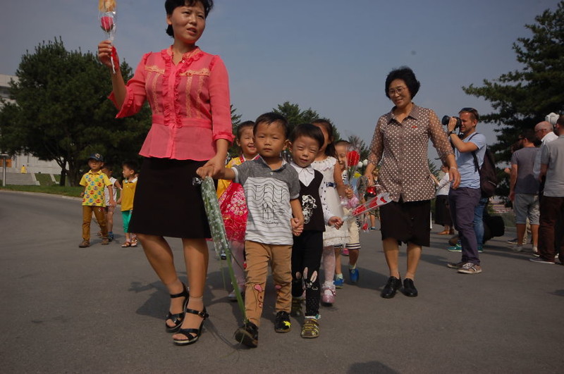 Группа детей несет цветы к памятнику товарищам Ким Ир Сену и Ким Чен Иру