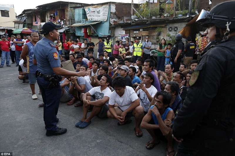 Жители города Pasig недалеко от ​​Манилы сидят на земле, а филиппинский полицейский разговаривает с ними о наркотиках  