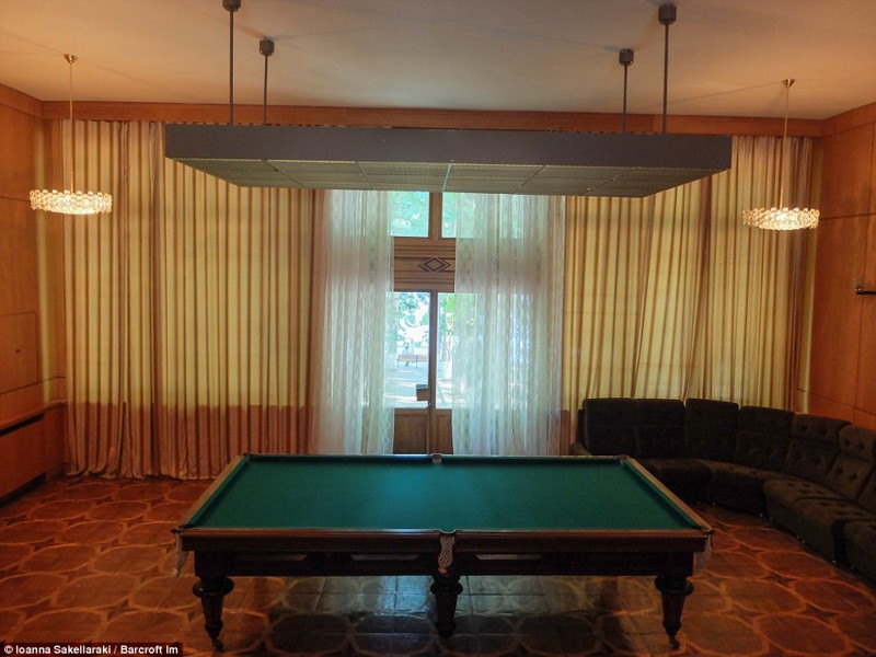 Игровая комната с деревянным бильярдным столом, окнами от потолка до пола и огромным диваном.