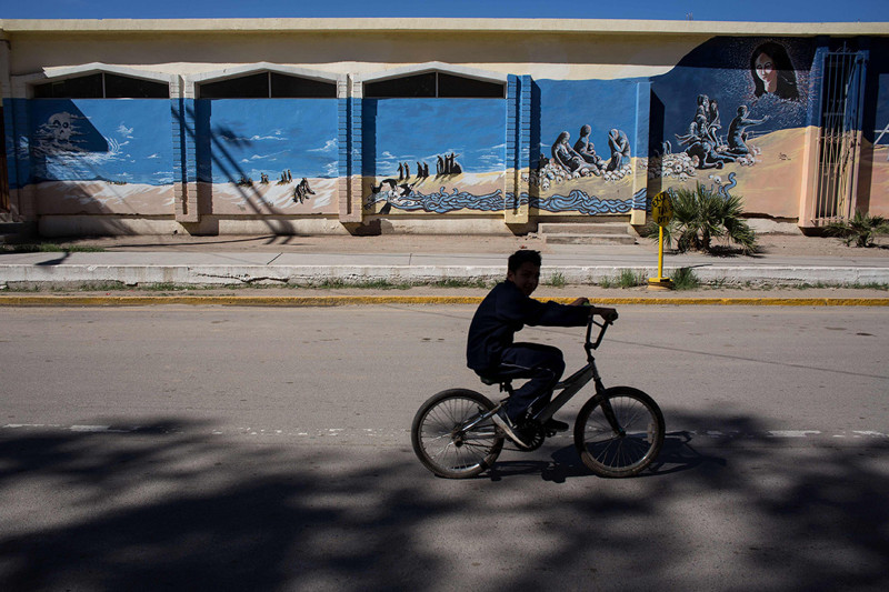 Мальчик на велосипеде проезжает настенную живопись, посвященную погибающим в пустыне мигрантам 