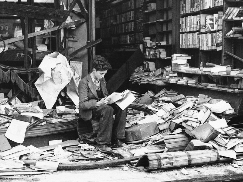 Мальчик сидит среди развалин лондонского книжного магазина после воздушного налета 8 октября 1940 года.
