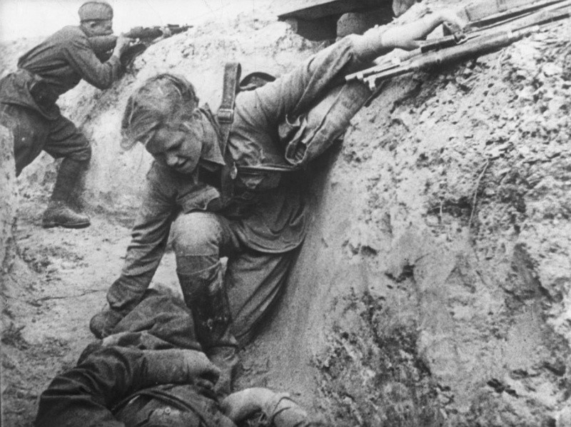 Советская санитарка оказывает помощь раненому красноармейцу под вражеским огнем.