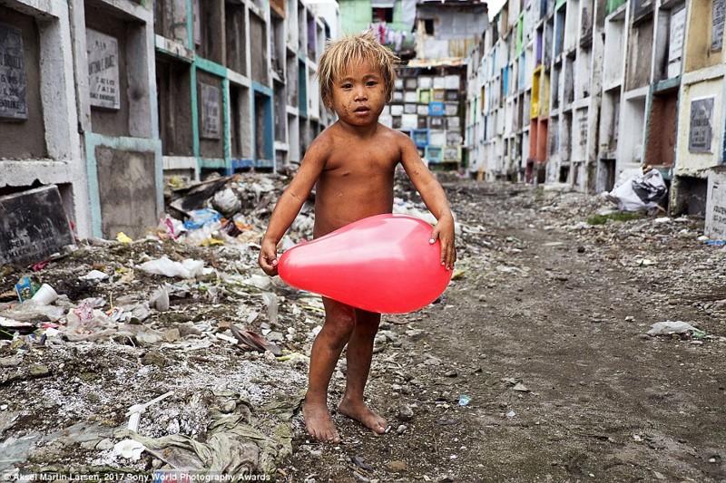 Портрет был сделан на кладбище в Маниле, Филиппины, где живет коммуна бездомных, включая и этого малыша. Он нашел среди костей воздушный шарик и теперь играет с ним