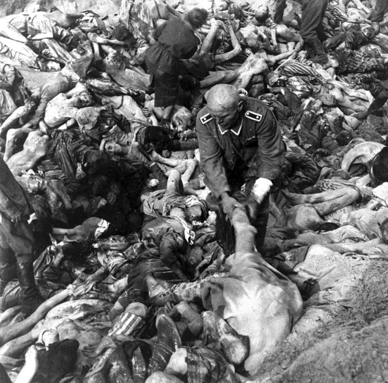 Немецкий СС  охранник, стоящий посреди сотен трупов, тащит тело жертвы  концлагеря в массовом захоронении в Бельзен, Германия, в  апреле 1945 года