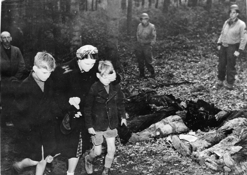 Немецкая женщина закрывает рукой глаза своему сыну, чтобы он  не видел погибших тел 57 русских солдат, которых убили  войска СС и бросили в братскую могилу до прибытия  американской армии.