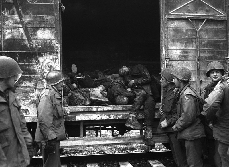 Американские  солдаты молча осматривают железнодорожные вагоны с мертвыми,  которые были обнаружены  на железнодорожной ветке в лагере  Дахау в Германии, 3 мая 1945 года.