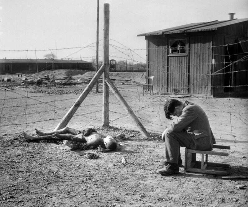 Молодой человек  сидит на перевернутом стуле рядом обгоревший труп в лагере  Текла возле Лейпцига, в апреле 1945 года.
