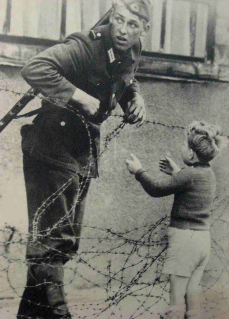 Солдат ГДР игнорирует приказ никого не пускать и помогает мальчику, оказавшемуся отделенным от своей семьи по ту сторону Берлинской стены. 1961 год.