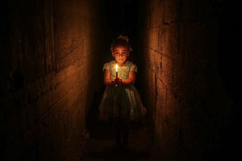 Палестинская девочка держит свечу, чтобы осветить дом после отключения электроэнергии в Джабалия в Газе, 27 июня 2017 года