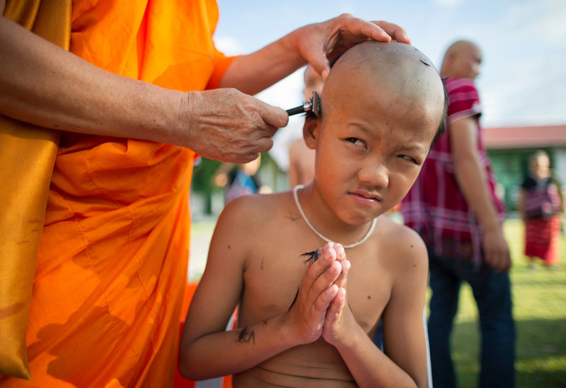 Буддийский монах сбривает волосы мальчику в Бангкоке, Таиланд, 23 июня 2017 года