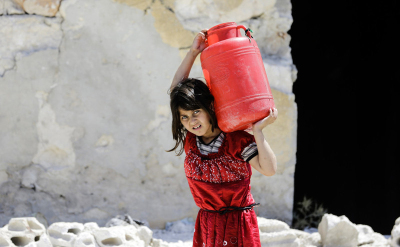 Сирийская девочка несет большой бак с водой в Алеппо 5 июля 2017 года