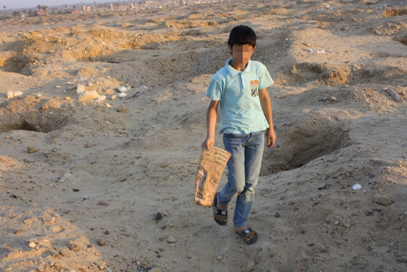 Ребенок с древним артефактом среди ям, вырытыми черными копателями на территории некрополя Абусир