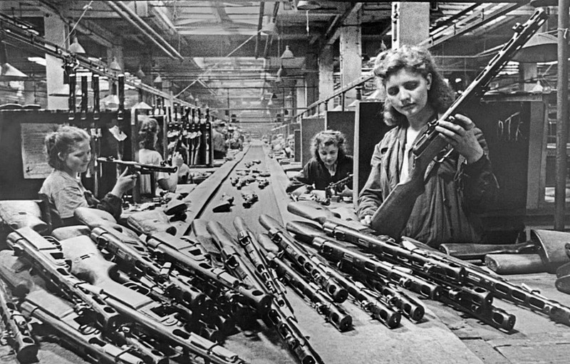 Женщины во время конвейерной сборки пистолетов-пулеметов ППШ на заводе в Москве. На переднем плане справа — бригадир комсомольско-молодежной бригады В. Баранова.