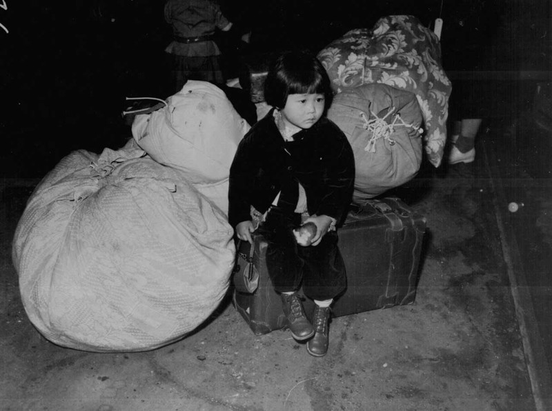 Маленькая японо-американская девочка ждёт автобус в лагерь интернирования японцев в США. Калифорния, апрель 1942 года. 