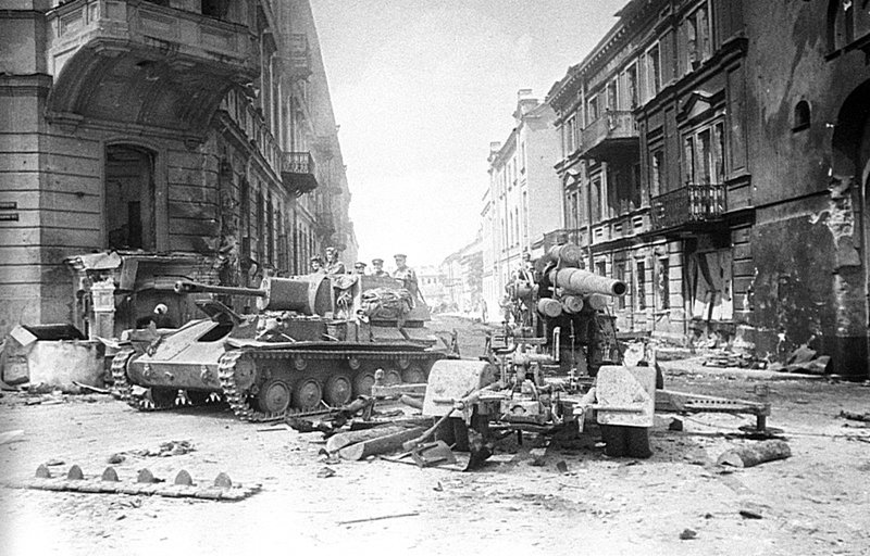 Советская САУ СУ-76М проезжает мимо разбитого 88-мм немецкого зенитного орудия (8,8 cm FlaK 18) в Вильнюсе. : июль 1944