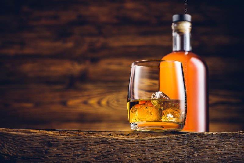 Стакан и бутылка виски на старом деревянном столе. Автор фото: Kamil Zabłocki