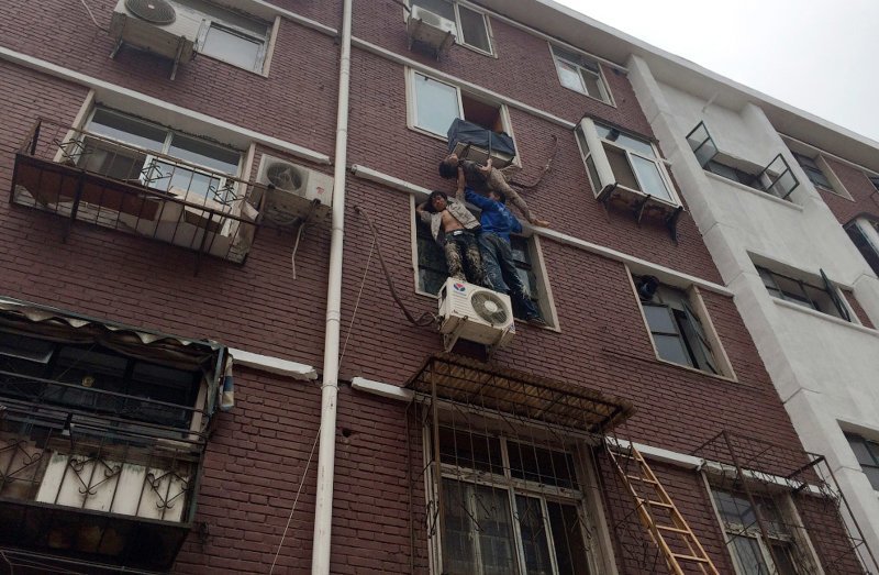 Опять Китай. Двое поддерживают женщину в ожидании спасателей, которая выпала из окна своей квартиры, по застряла в крепеже кондиционера