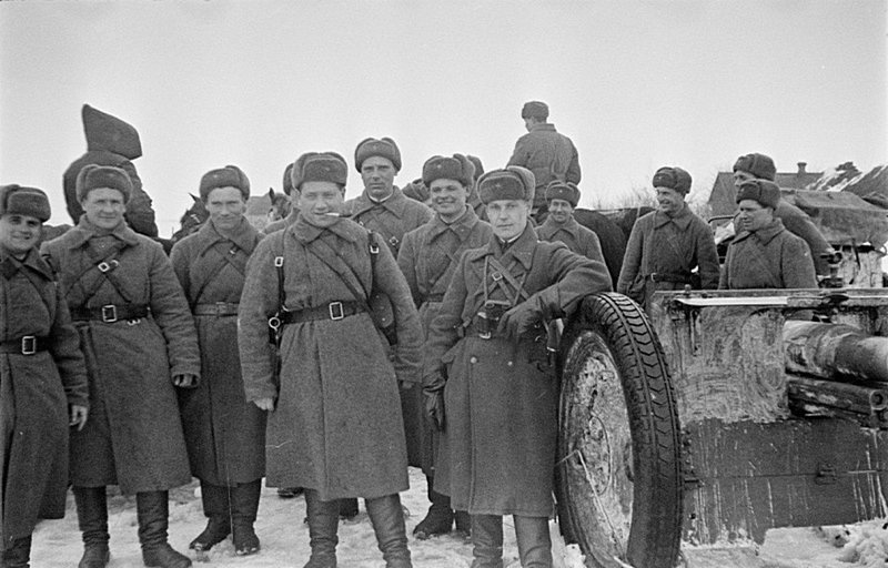 Групповой снимок советских офицеров и солдат рядом с 76-мм полковой пушкой образца 1943 года в населенном пункте.
