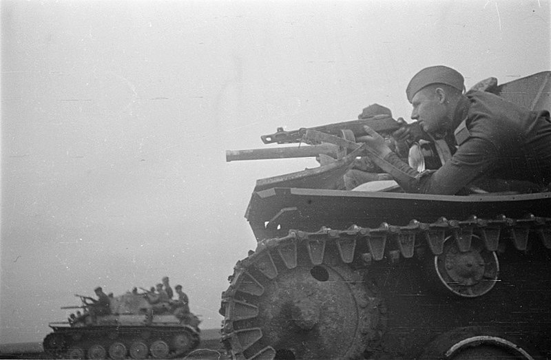 Советский солдат прицеливается из пистолет-пулемета, лежа на броне танка Т-70.