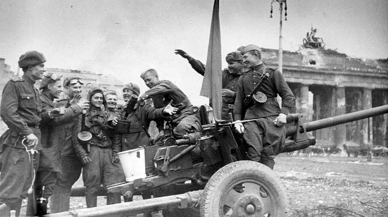 Артиллеристы, танкисты и пехотинцы Красной армии возле 76-мм пушки ЗиС-3 выпивают за Победу у Бранденбургских ворот в Берлине.