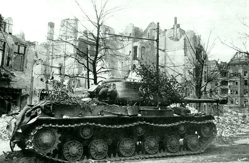 Советский танк ИС-2 на разрушенной улице Берлина. На машине видны элементы маскировки. Германия, апрель 1945