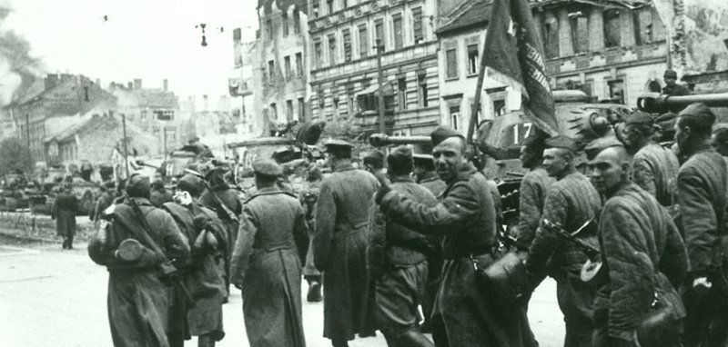 Советские бойцы с красным знаменем проходят возле колонны танков ИС-2 на улице Берлина. Германия, апрель-май 1945 