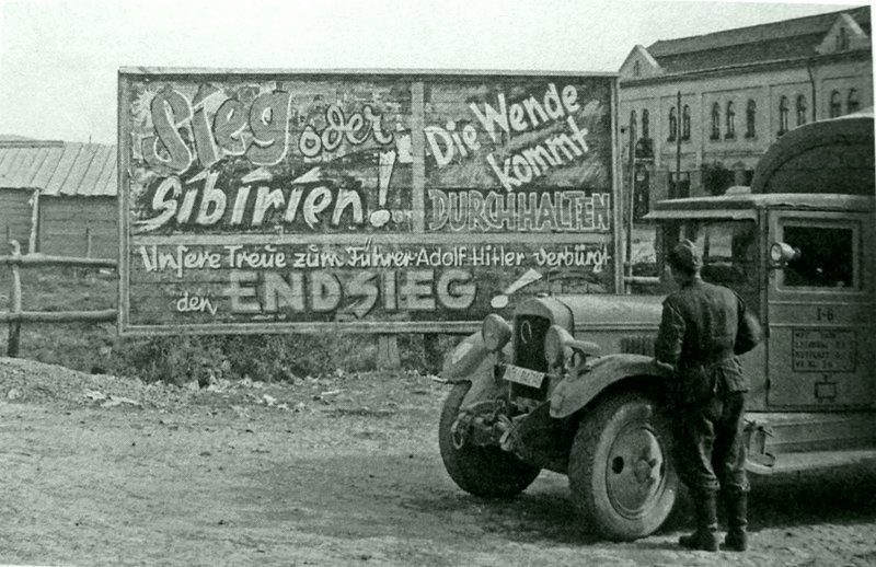 Немецкий солдат у трофейного грузовика ЗиС-5 смотрит на щит с лозунгами в Северной Трансильвании.  Место съемки: Венгрия.  Время съемки: август 1944.