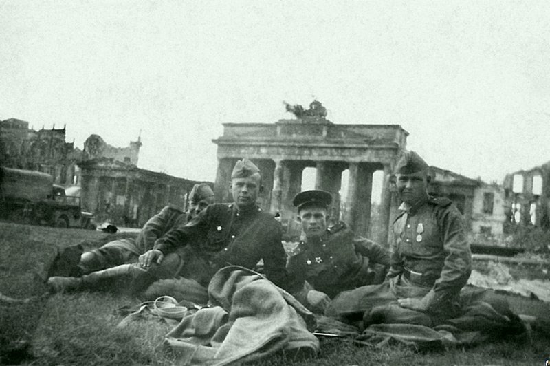Группа советских воинов-артиллеристов отдыхает на траве у Бранденбургских ворот.  Место съемки: Берлин, Германия. Время съемки: 1945