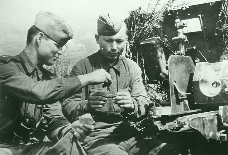 Советские артиллеристы крутят цигарки у замаскированной 76-мм дивизионной пушки ЗиС-3. Время съемки: 1943.   