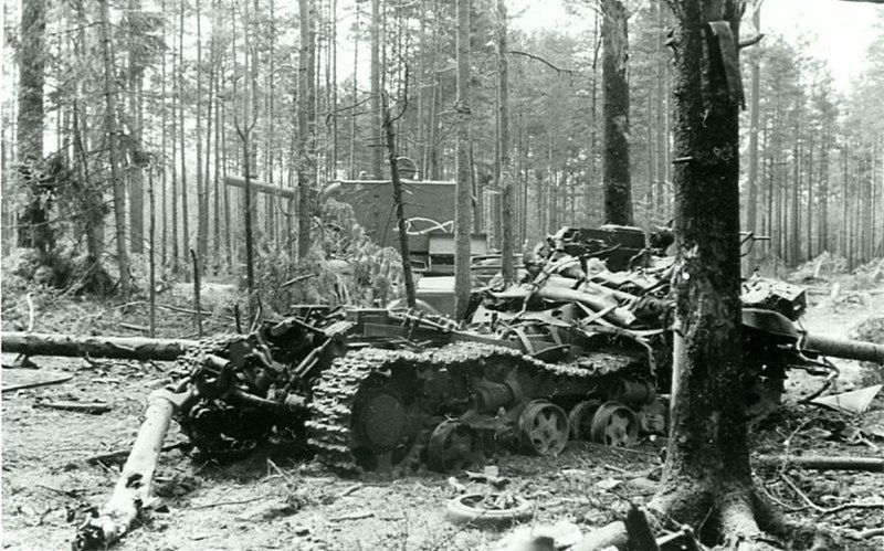 Взорванный в лесу брошенный советский гусеничный тягач СТЗ-5-НАТИ. За тягачом стоит брошенный тяжелый танк КВ-2 выпуска мая — июня 1941 года из одной из танковых дивизий 7-го механизированного корпуса Западного фронта. 