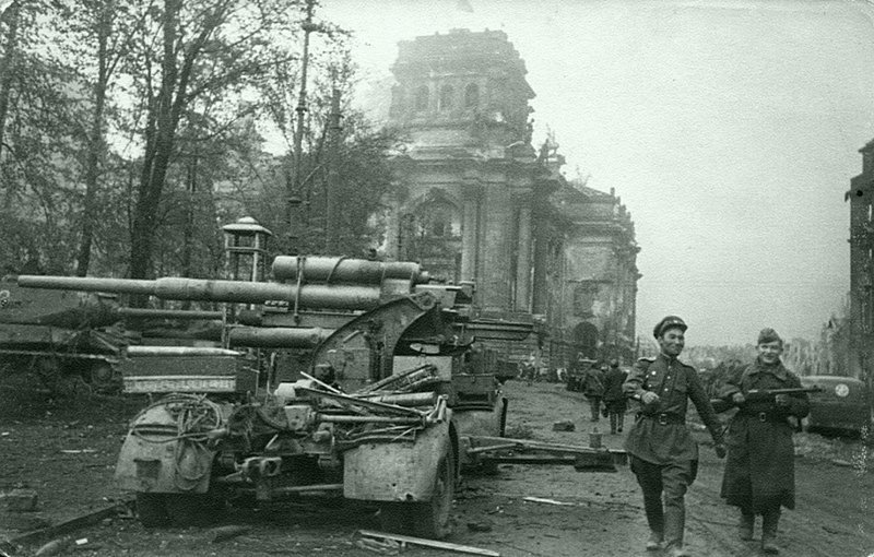 40. Советские бойцы проходят возле немецкой 88-мм зенитки Flak 37 у здания Рейхстага в поверженном Берлине. Слева от зенитки стоит советский танк ИС-2.