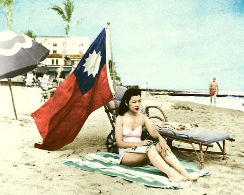Рут Ли, хозяйка в китайском ресторане, сидит под китайским флагом, чтобы её не приняли за японку, когда она загорает на своих выходных в Майами. 15 декабря 1941 г. 