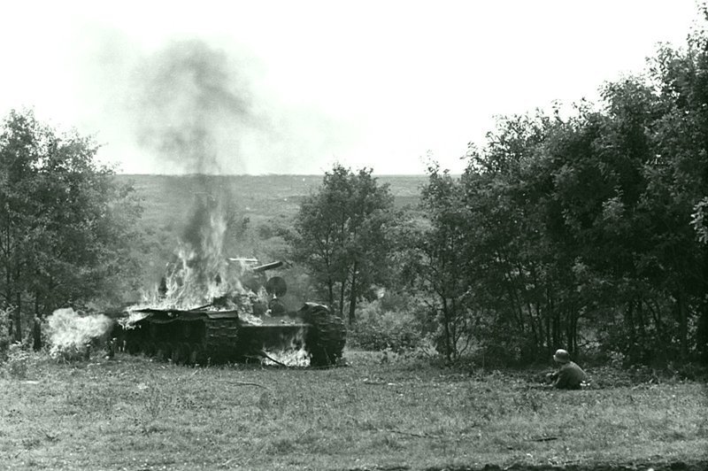 Подбитый и горящий советский танк КВ-1 и сидящий в окопе венгерский солдат. 