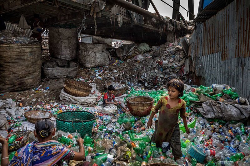 Под мостом реки Буриганга в Бангладеш семья удаляет этикетки с пластиковых бутылок, сортирует зеленые и прозрачные бутылки и продет торговцу утилем. В среднем сборщики мусора зарабатывают 100 долларов в месяц.