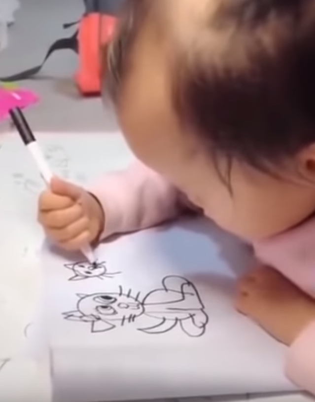 Маленькая девочка с трудом удерживает в руке фломастер, но рисует получше взрослых