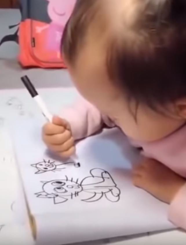 Маленькая девочка с трудом удерживает в руке фломастер, но рисует получше взрослых