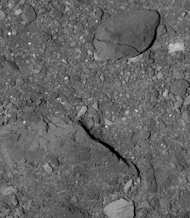 Поверхность Бенну к югу от экватора. Крупный валун с трещиной имеет длину 21 метр. Ниже видна видна формация, уходящая вглубь поверхности.