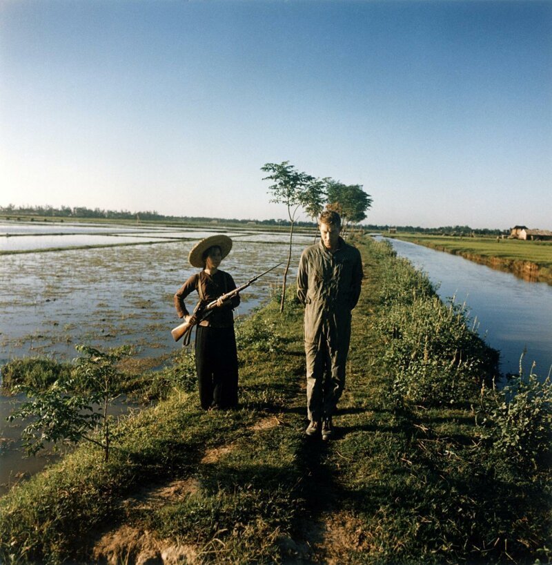 Пойманный в плен американский майор Дьюи Уодделл охраняется милиционеркой с оружием и штыком на рисовом поле. Вьетнам, 1967 . 