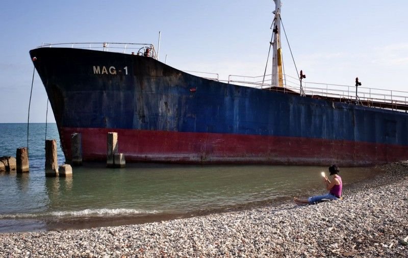Девушка прихорашивается. На заднем фоне — танзанийский торговый корабль, севший на мель еще в 2010 году. Сухуми, Абхазия.