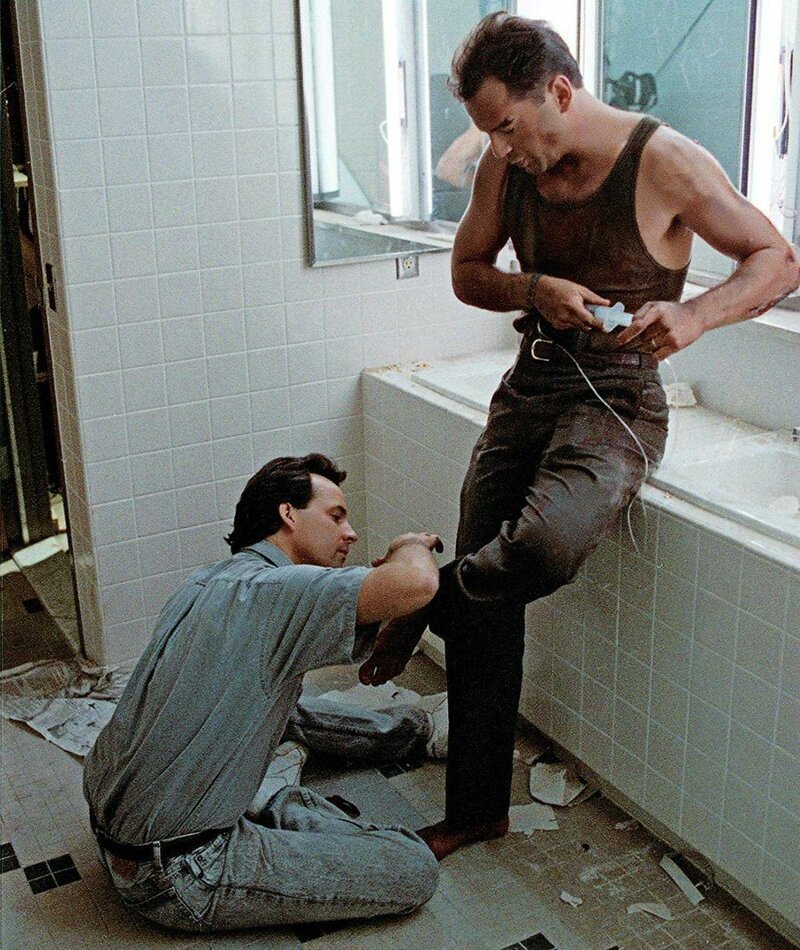 Скотт Х. Эддо мажет поддельной кровью ногу Брюса Уиллиса на съемочной площадке фильма «Крепкий орешек»