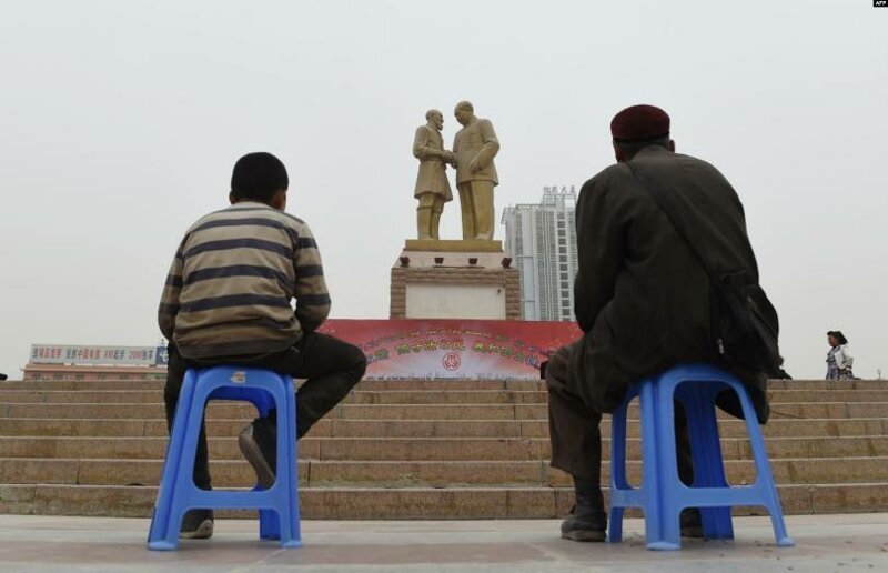 Отец и сын, уйгуры, в центре местной столицы Урумчи смотрят на огромную статую «Мао встречает уйгура»