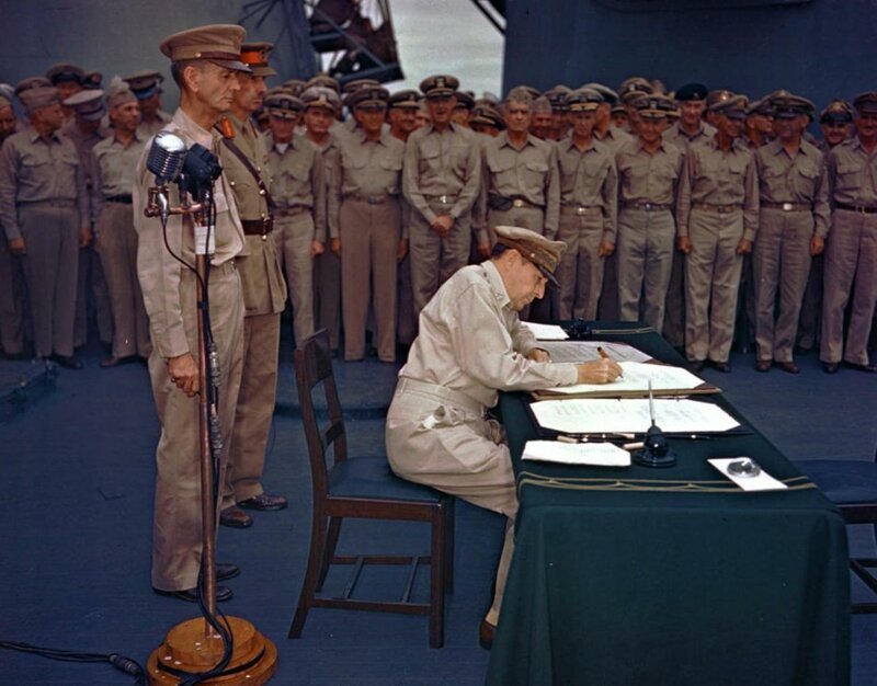  Генерал Дуглас Макартур подписывает акт о капитуляции Японии на борту линкора «Миссури». Слева от Макартура, на переднем плане — генерал-лейтенант Джонатан Уэйнрайт, за ним — британский генерал-лейтенант А.Е.Персиваль, 2 сентября 1945 года.  Уэйнрай